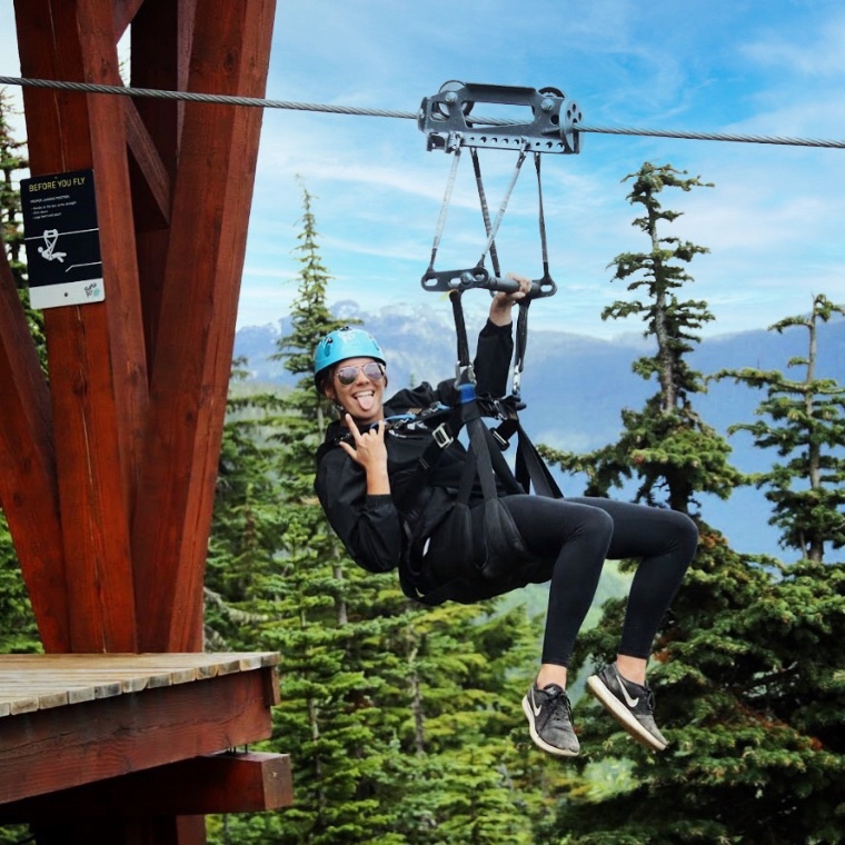 Lauren Tomsich riding on a zipline with mountains and trees in the background.